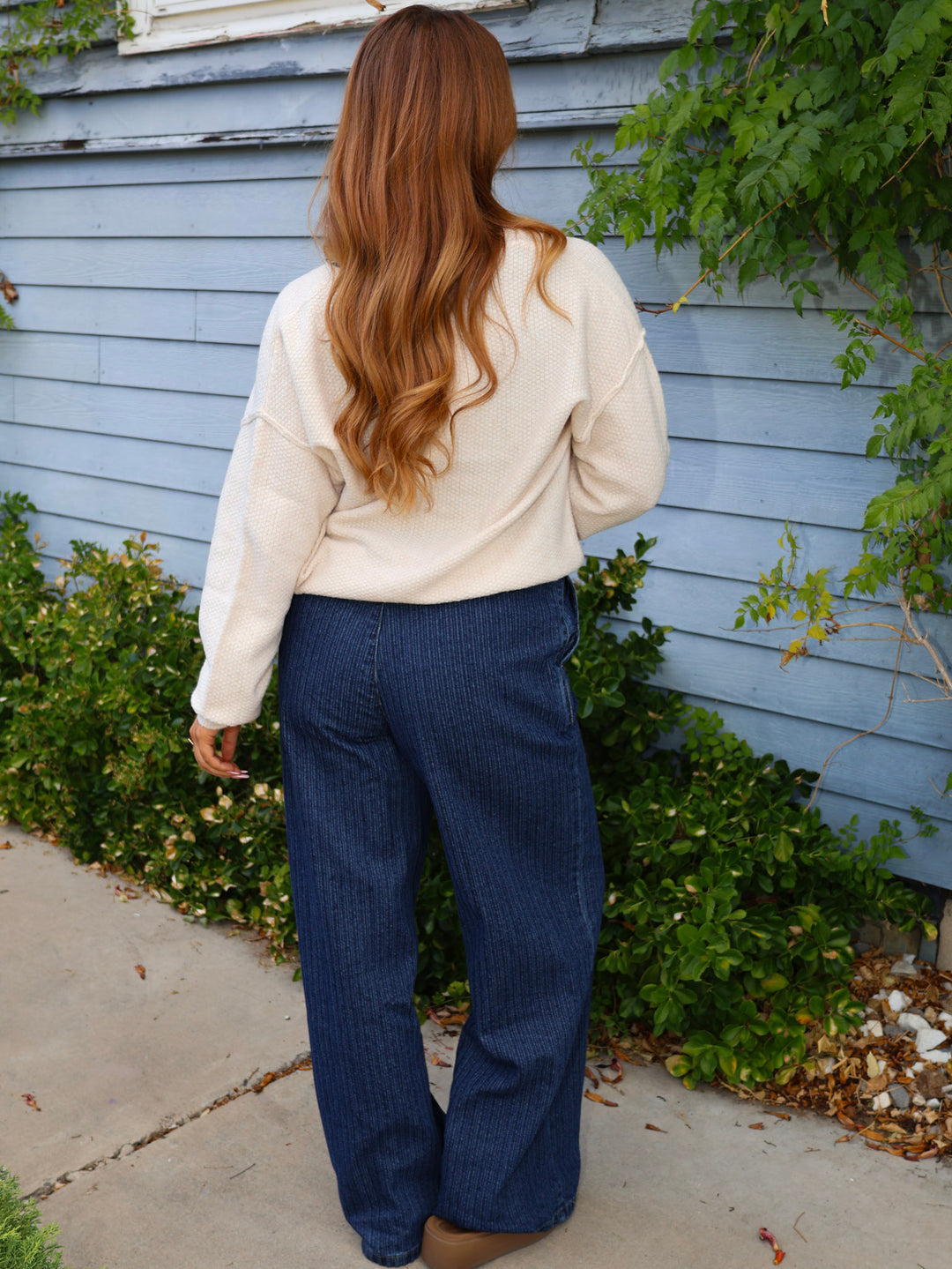 Person wearing a white sweater and blue pants standing in front of a blue house.