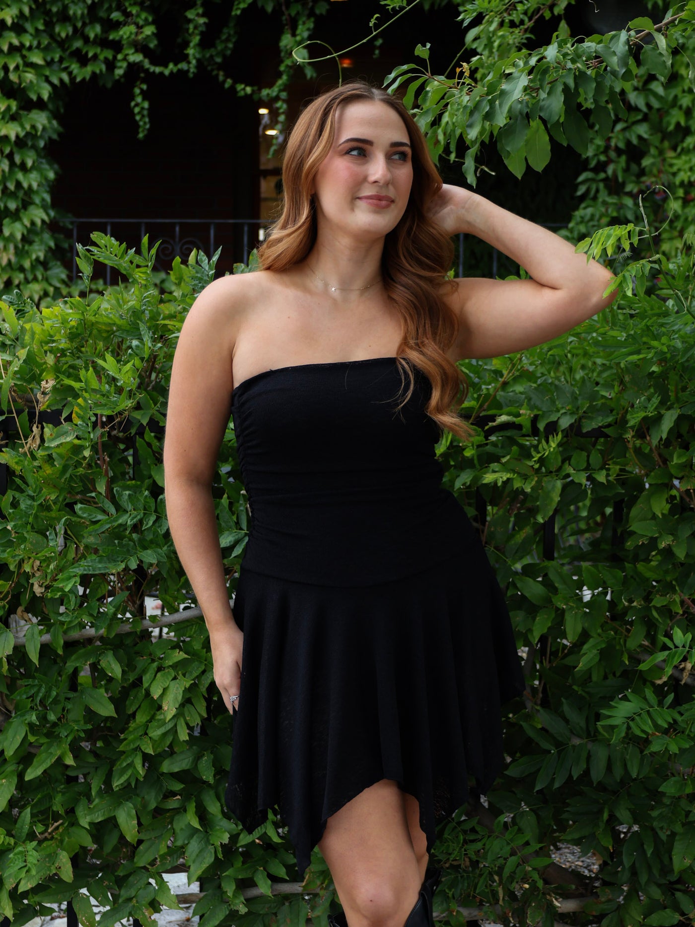 Woman wearing a black strapless dress standing in front of green foliage