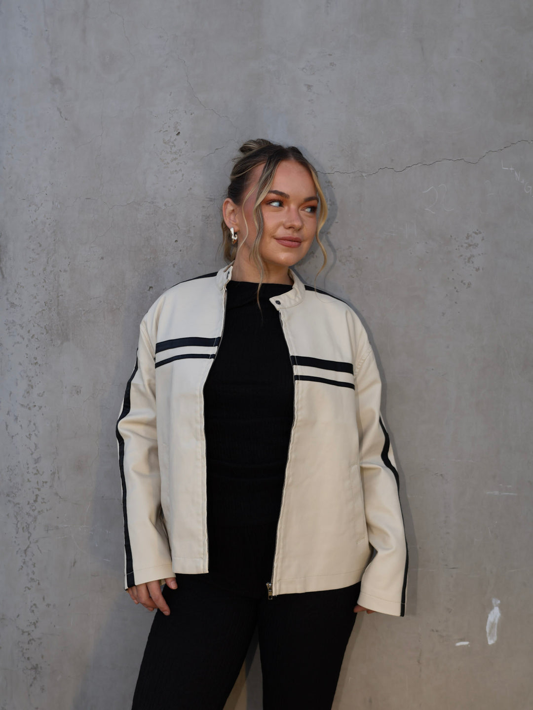 Person wearing a white jacket with black accents against a gray wall