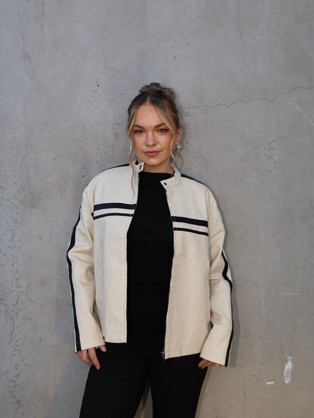 Woman wearing a white jacket with black stripes against a gray concrete wall