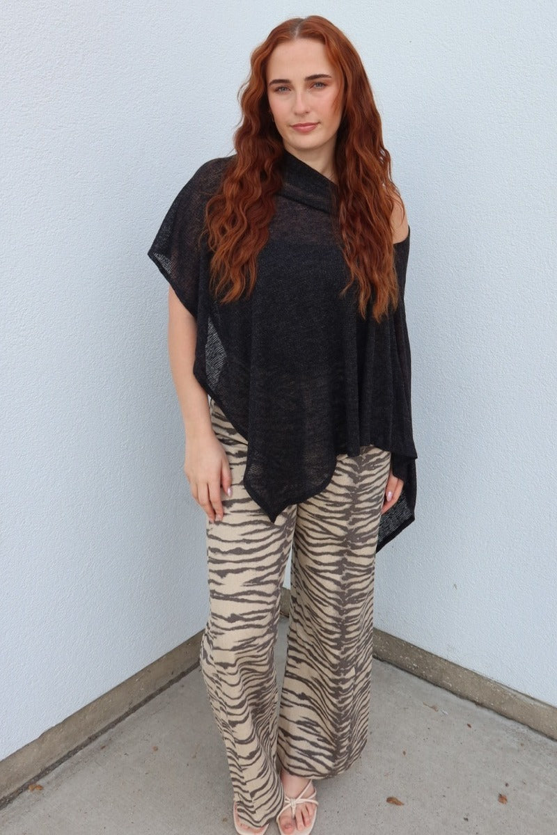 Model wearing the black Portofino sheer knit poncho top with tiger stripe wide leg pants, full length front view