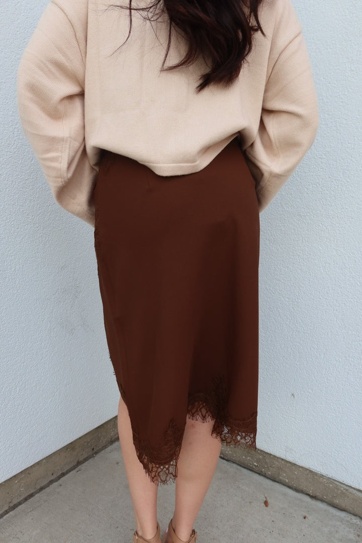 Close back view of the brown Lucy asymmetric lace trim satin midi skirt with the lace trim at the hem