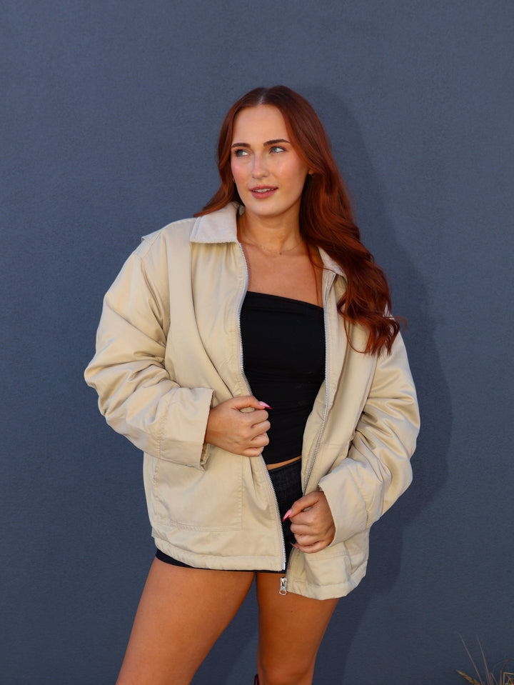 Woman wearing a beige jacket over a black top against a blue background