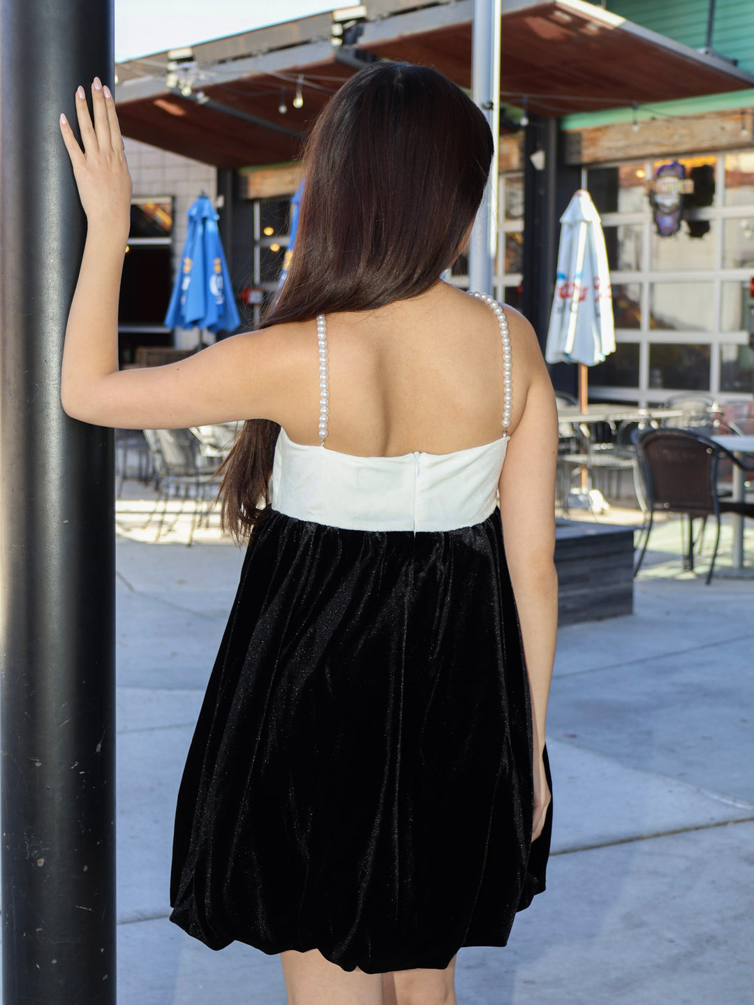Woman wearing a black and white dress standing outdoors near a building entrance.
