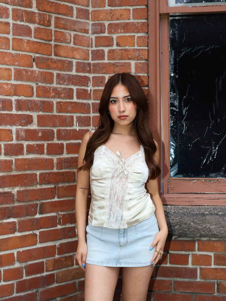 Woman standing against a brick wall wearing a white top and denim shorts.