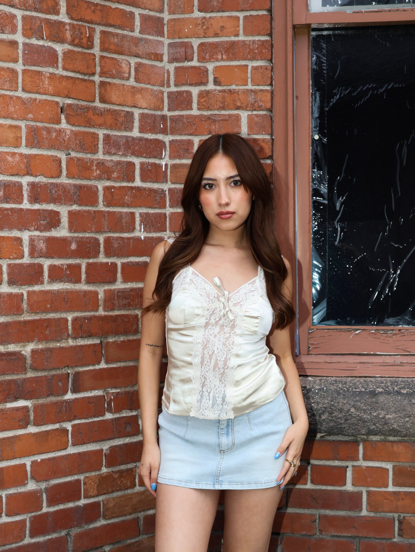 Woman standing against a brick wall wearing a white top and denim shorts.
