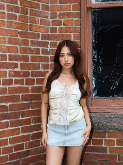 Woman standing against a brick wall wearing a white top and denim shorts.