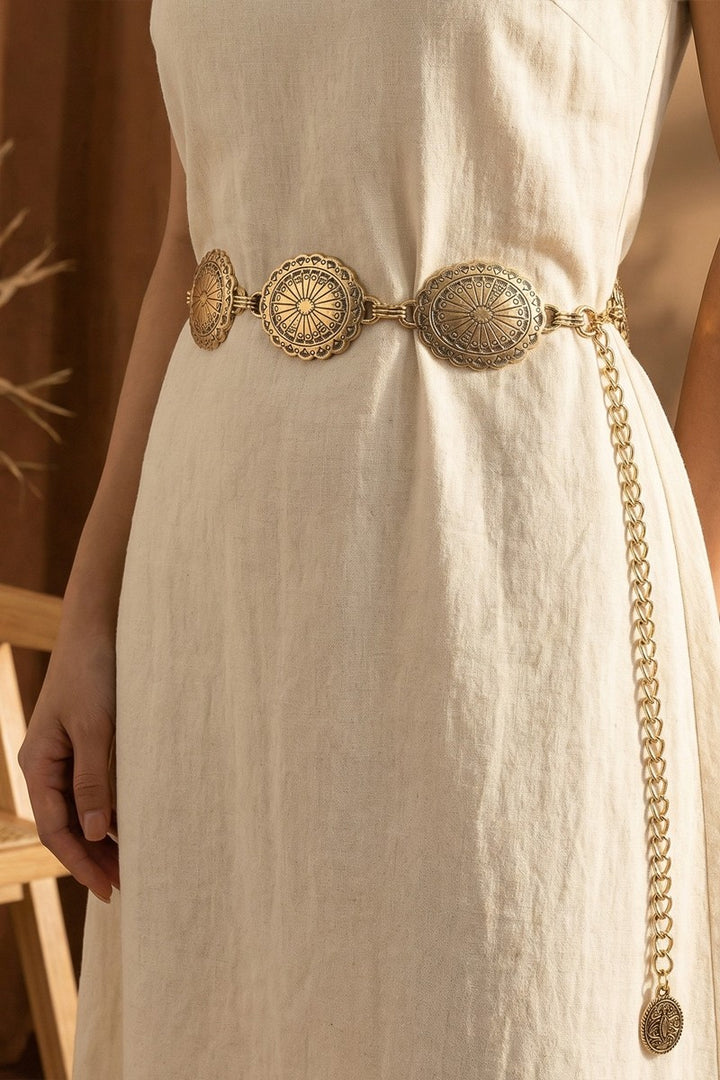 The Concho Disc Chain Belt in Antique Gold - Styled on Model at Waist Over Cream Linen Dress Showing Ornate Concho Discs, Chain Links & Dangling Charm Pendant