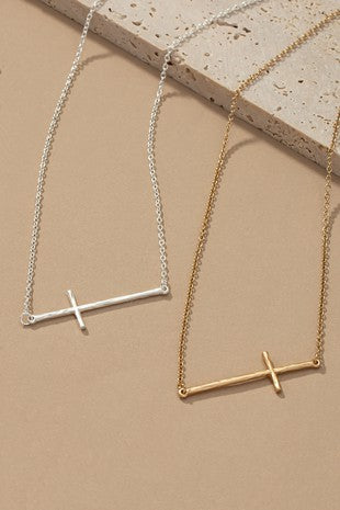 Two necklaces, one with a silver sideways cross and the other with a gold sideways cross, laid on a textured surface.