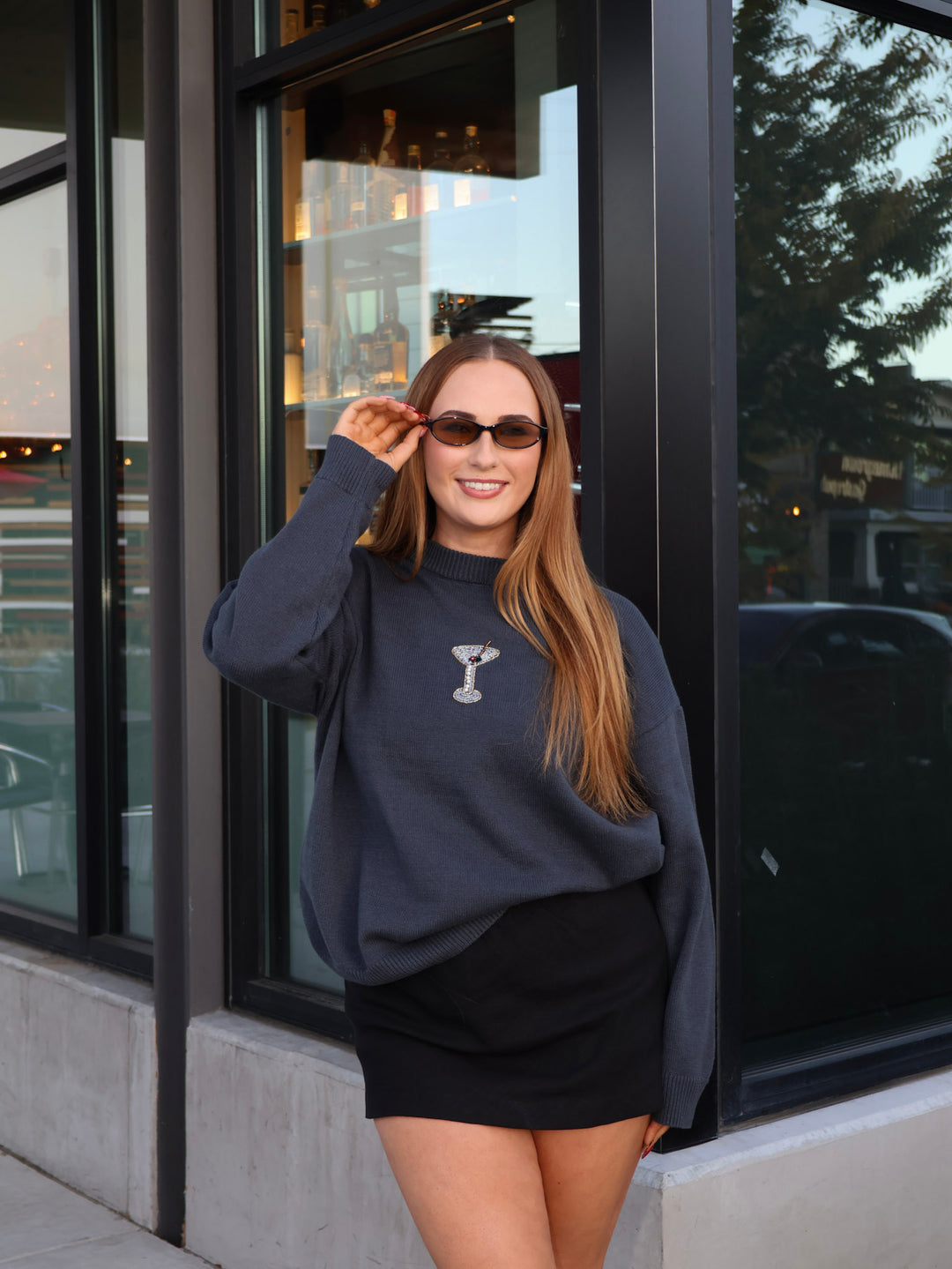 Woman wearing a navy sweatshirt with a logo and sunglasses, standing outside a building.
