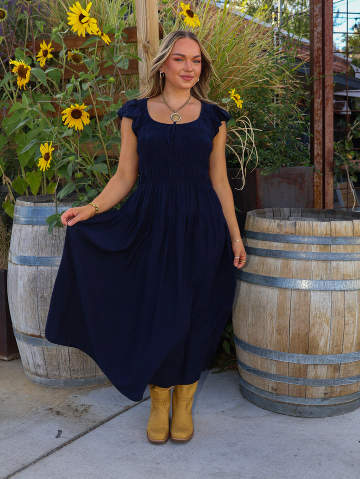 Woman in a navy dress standing next to wooden barrels with sunflowers in the background