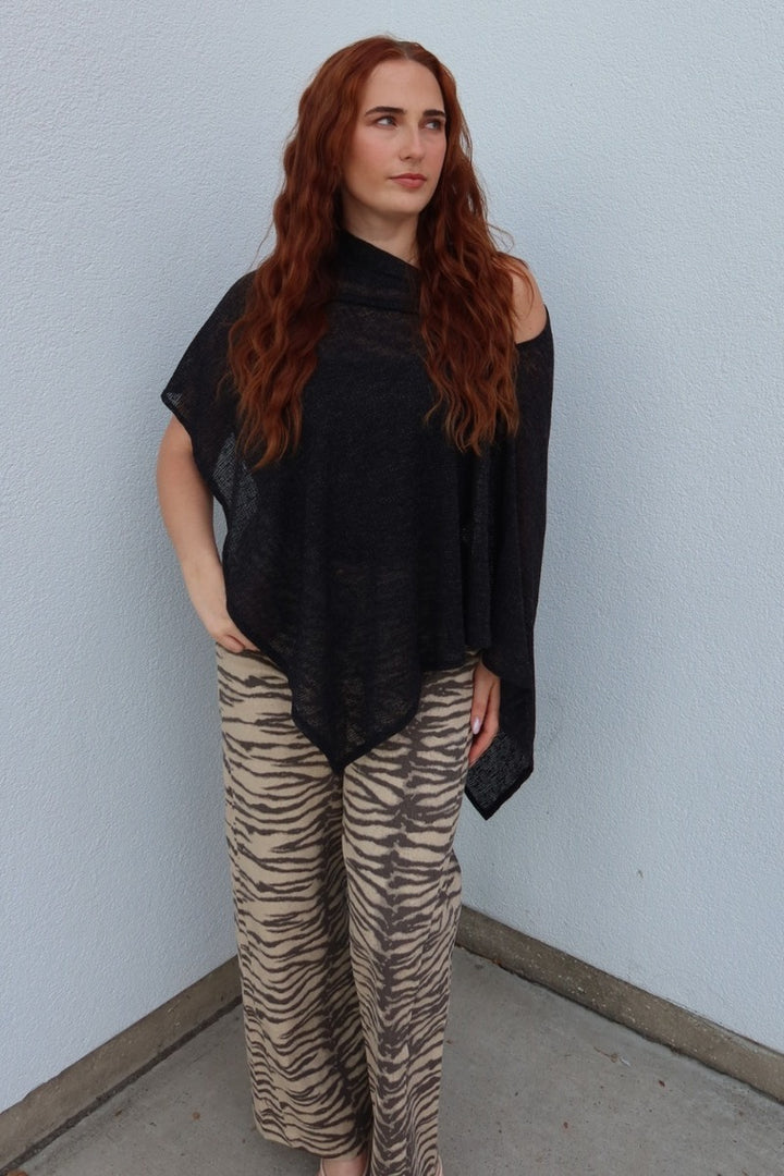 Model in the black Portofino sheer knit poncho top, hand in pocket, worn over tiger stripe wide leg pants