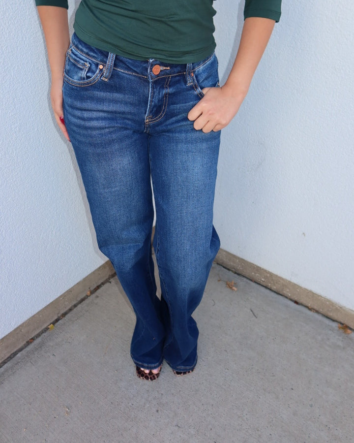 Close-up of the Waltman low rise dark wash wide leg jeans worn with a green top, hand in pocket