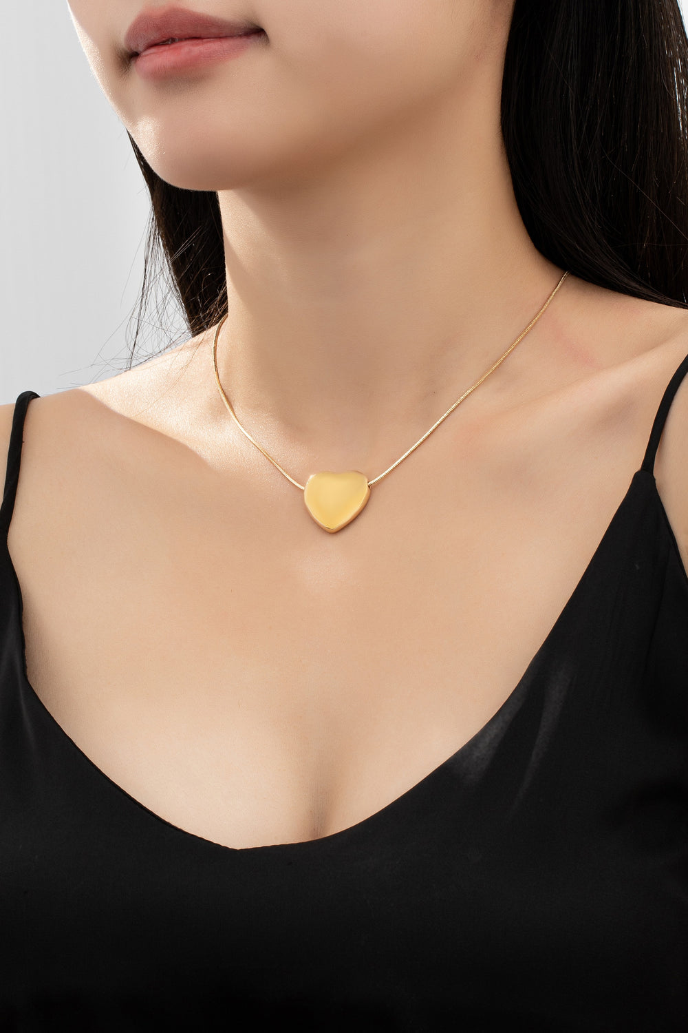 Gold necklace with a heart-shaped pendant worn by a person in a black top.