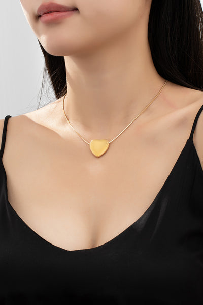 Gold necklace with a heart-shaped pendant worn by a person in a black top.