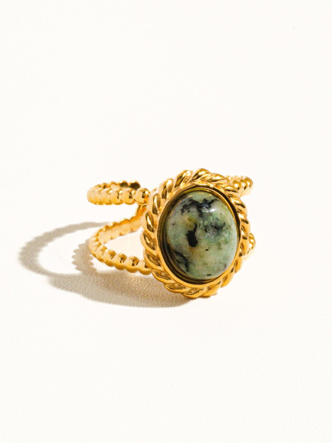 The Peacock Stone Rope Bezel Double Band Ring in 18K Gold - Three-Quarter Product Shot on Cream Background Showing Rope-Twist Bezel Detail, Speckled Green Peacock Stone & Double Band Profile