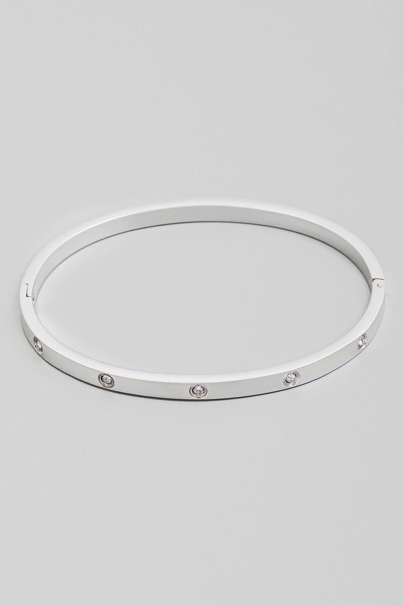 The CZ Studded Hinged Bangle Bracelet in Silver - Product Shot on Grey Background Showing Sleek Silver Tone Flat Profile Bangle with Evenly Spaced Flush-Set Round CZ Stones & Hinged Clasp