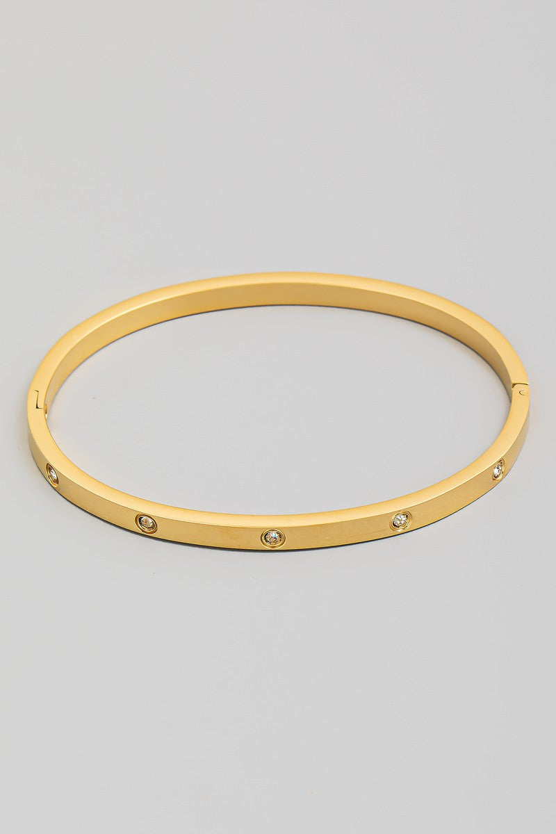 The CZ Studded Hinged Bangle Bracelet in Gold - Product Shot on Grey Background Showing Sleek Gold Tone Flat Profile Bangle with Evenly Spaced Flush-Set Round CZ Stones & Hinged Clasp