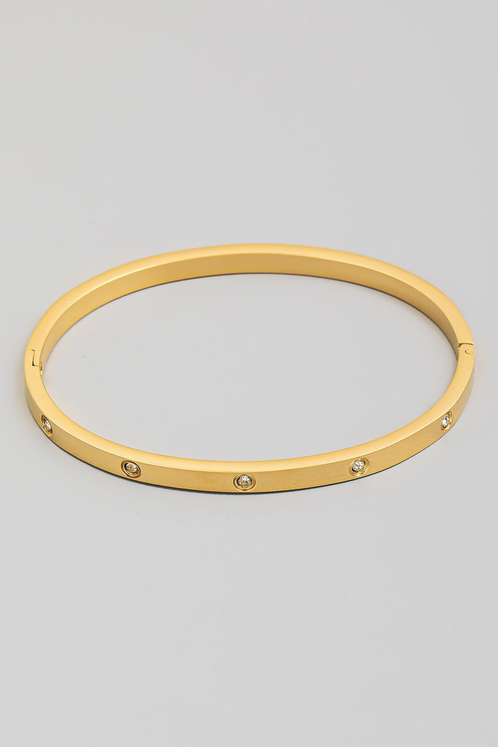 The CZ Studded Hinged Bangle Bracelet in Gold - Product Shot on Grey Background Showing Sleek Gold Tone Flat Profile Bangle with Evenly Spaced Flush-Set Round CZ Stones & Hinged Clasp