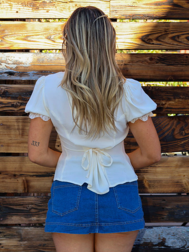 Woman wearing a white blouse and blue skirt standing against a wooden wall.