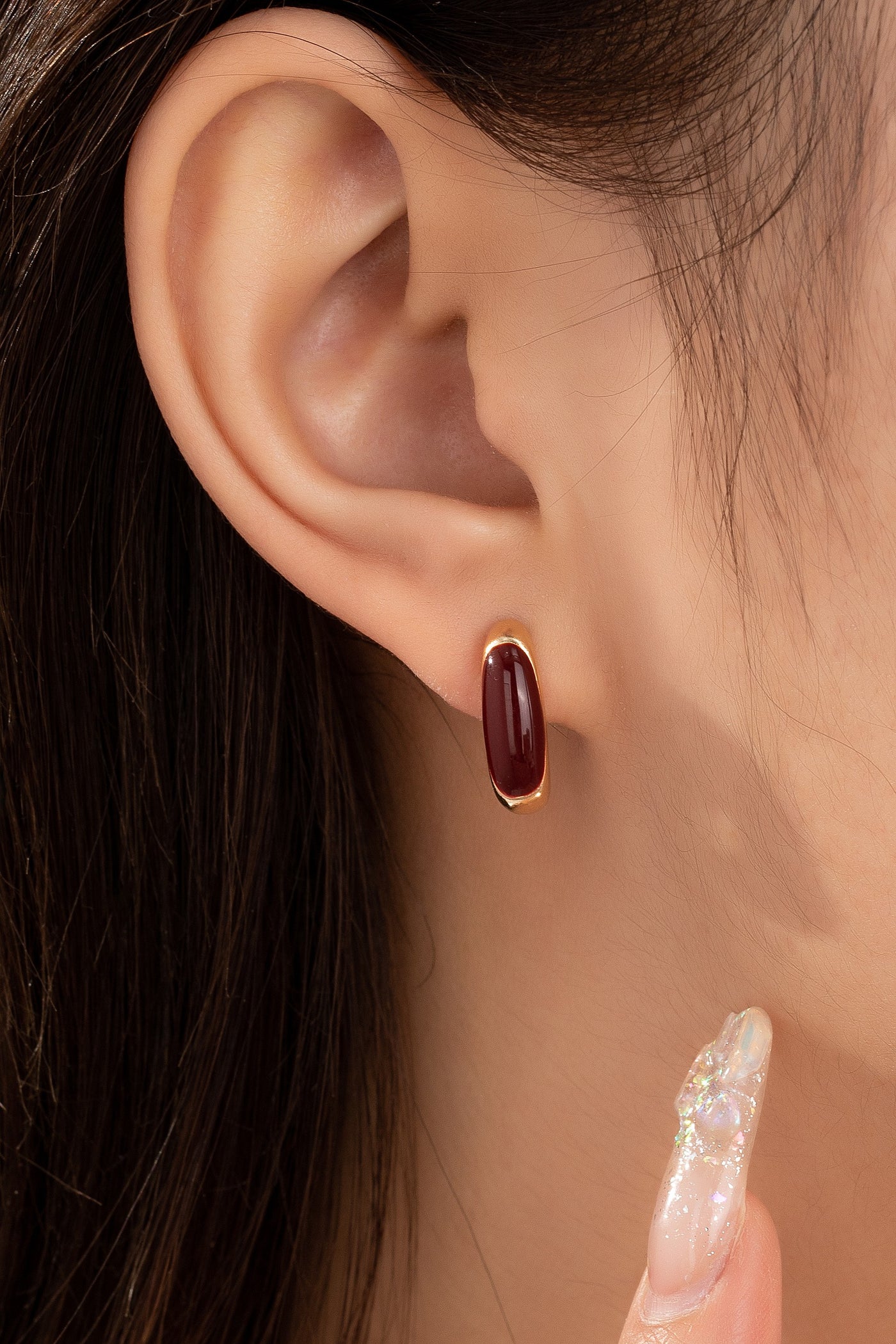 Close-up of an ear wearing a burgundy earring with a blurred background