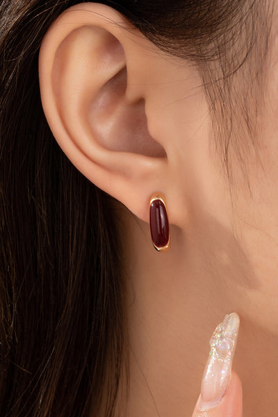 Close-up of an ear wearing a burgundy earring with a blurred background
