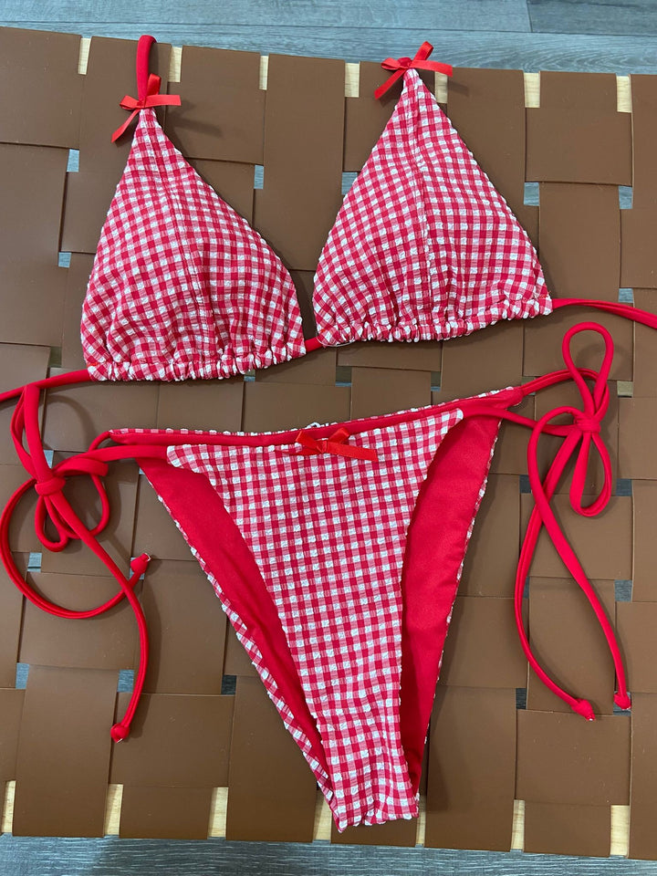 The Cherry Gingham Triangle Bikini Set - Flat Lay on Rattan Surface Showing Full Set Detail — Gingham Seersucker Texture, Bow Tie Details & Red Side Tie Bottoms