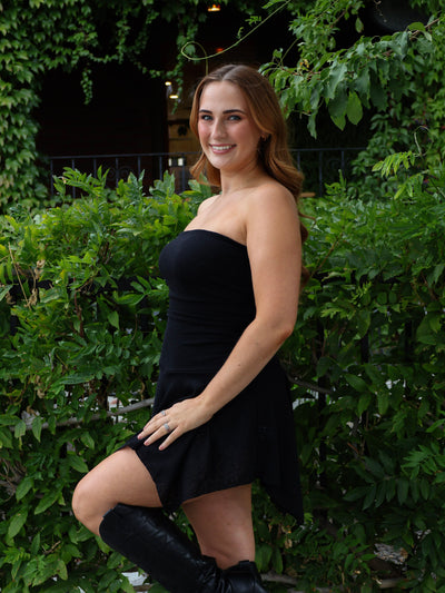Woman in a black dress standing outdoors with greenery in the background