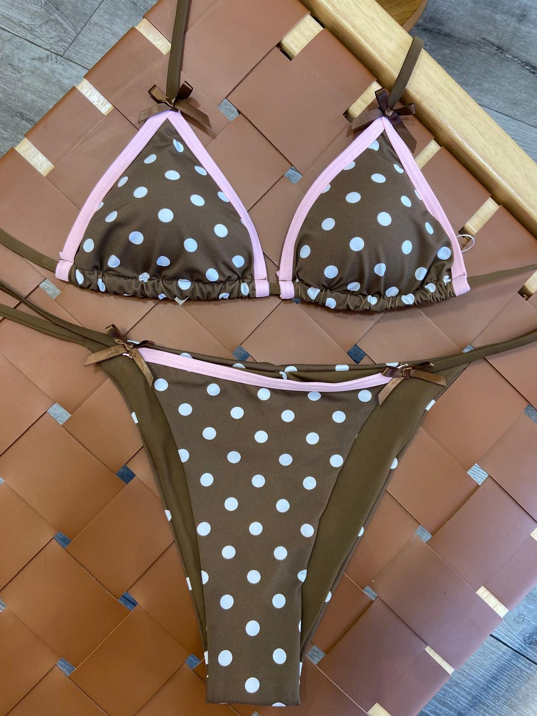 The Café Polka Bikini Set - Flat Lay on Rattan Surface Showing Full Set Detail — Brown Polka Dots, Blush Pink Piping, Bow Decor & Tie-Side Bottoms