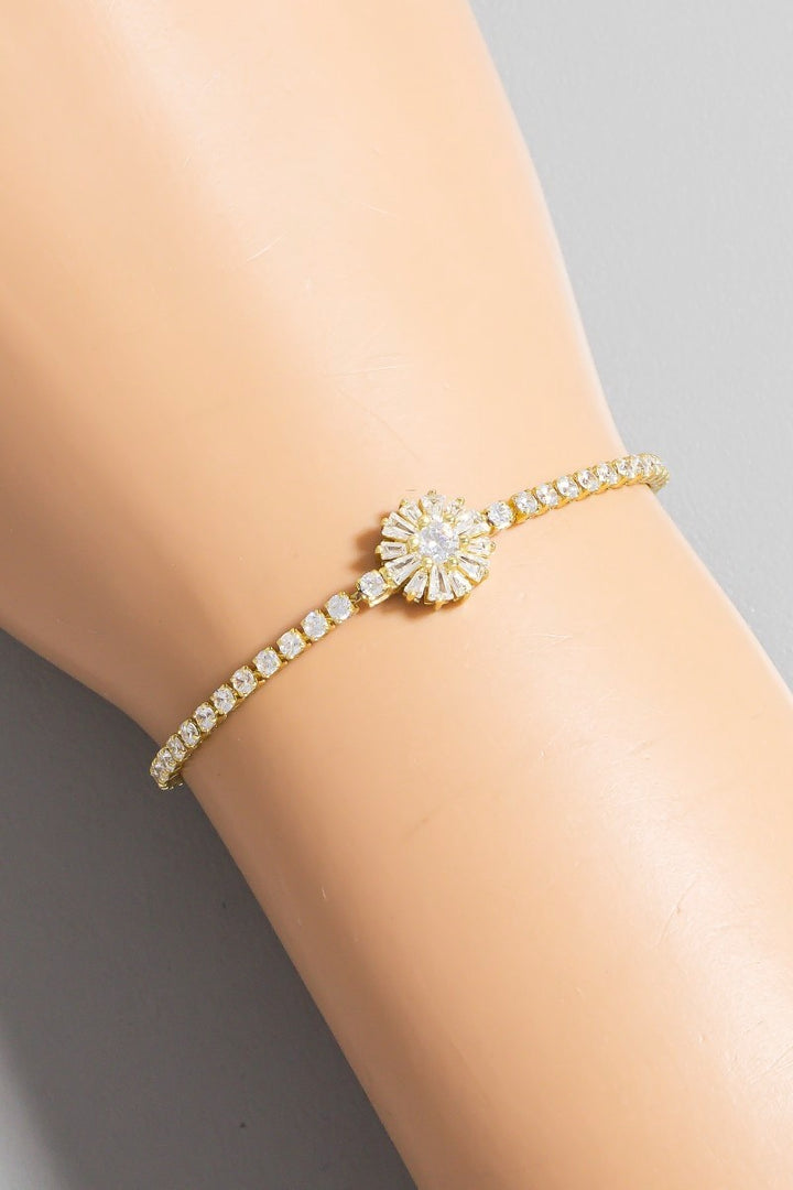 Gold bracelet with a sunflower design on a person's wrist against a neutral background