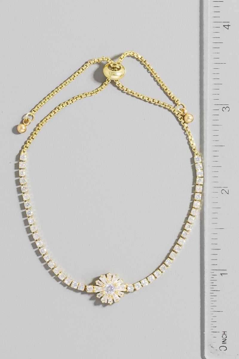 Gold bracelet with a floral clasp next to a ruler on a gray background