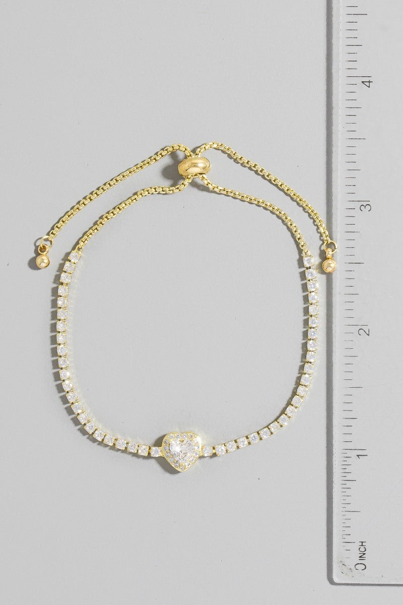 Gold bracelet with a heart-shaped clasp next to a ruler on a gray background