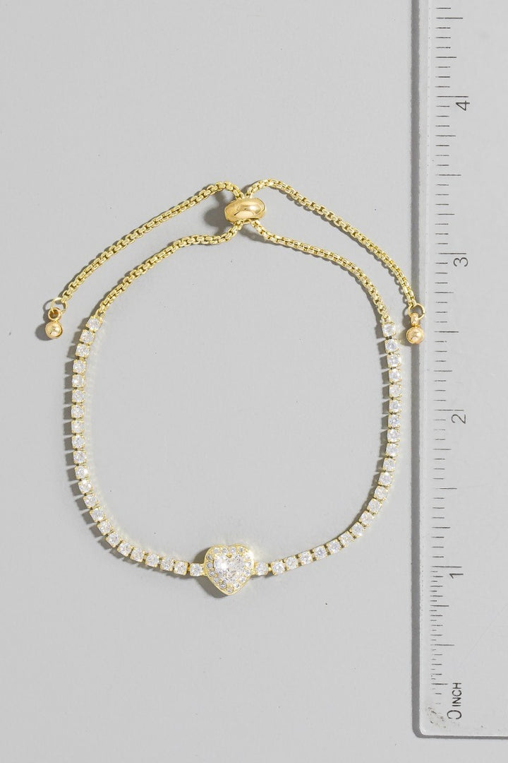 Gold bracelet with a heart-shaped clasp next to a ruler on a gray background