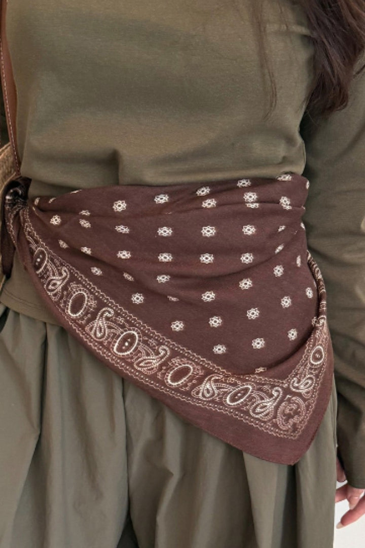 A brown bandana with white floral and paisley patterns wrapped around the waist of a person wearing an olive green dress.