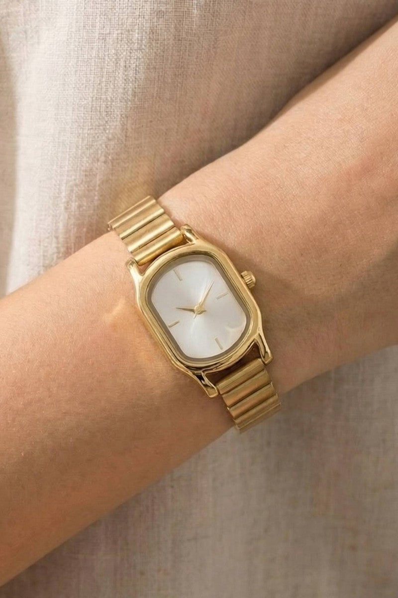 The Cushion Rectangle Bangle Watch in Gold - On-Model Wrist Shot Showing Gold Cushion Rectangle Case with Pearl White Dial & Ribbed President-Style Bracelet Band Against Cream Linen