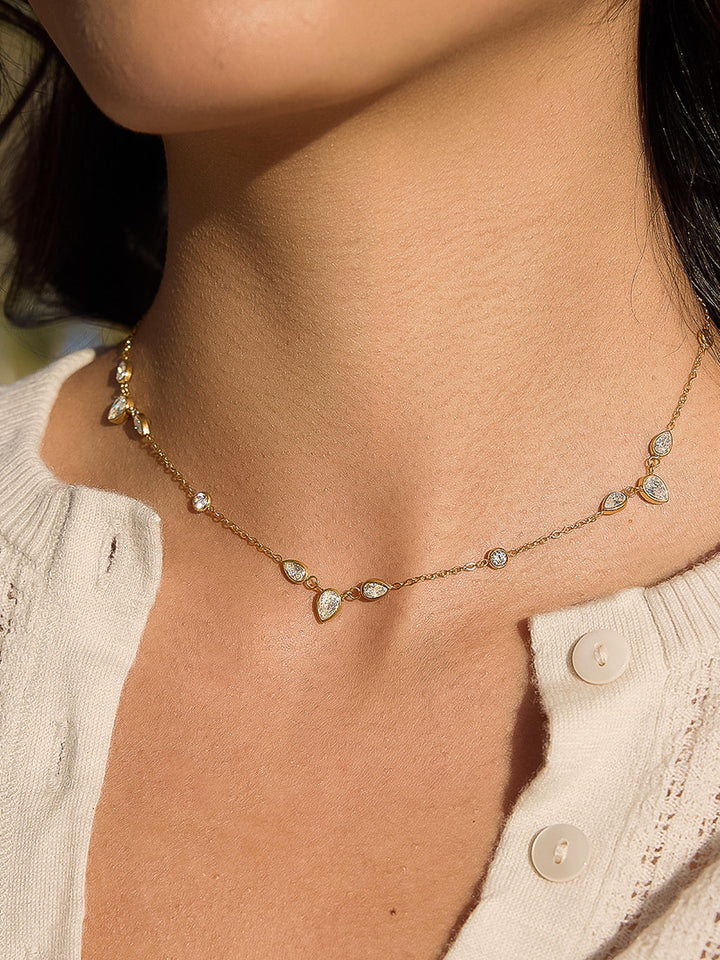 The CZ Teardrop Station Layering Necklace in 18K Gold - On-Model Close-Up Showing Alternating Round & Teardrop CZ Bezel Stations on Fine Gold Cable Chain at Collarbone Against Warm Skin & Cream Knit