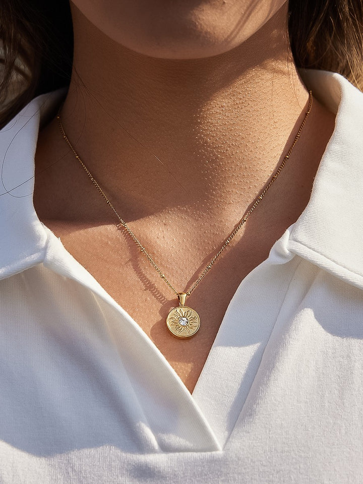 The CZ Sun Medallion Coin Necklace in 18K Gold - Outdoor On-Model Lifestyle Shot Showing Sun Medallion Coin Pendant on Satellite Chain at Collarbone in Natural Sunlight Against White Linen Shirt