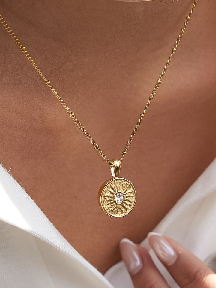The CZ Sun Medallion Coin Necklace in 18K Gold - On-Model Close-Up Showing Round Engraved Sun Coin Pendant with CZ Center Stone on Satellite Curb Chain at Collarbone Against Warm Skin & White Top