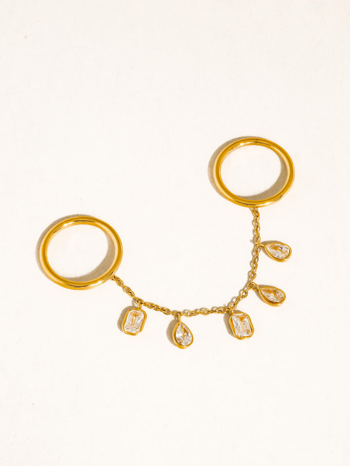 The CZ Dangle Chain Double Ring in 18K Gold - Product Flat Lay on White Background Showing Both Polished Gold Bands, Delicate Chain Connector & Five Mixed-Cut CZ Bezel Dangle Charms