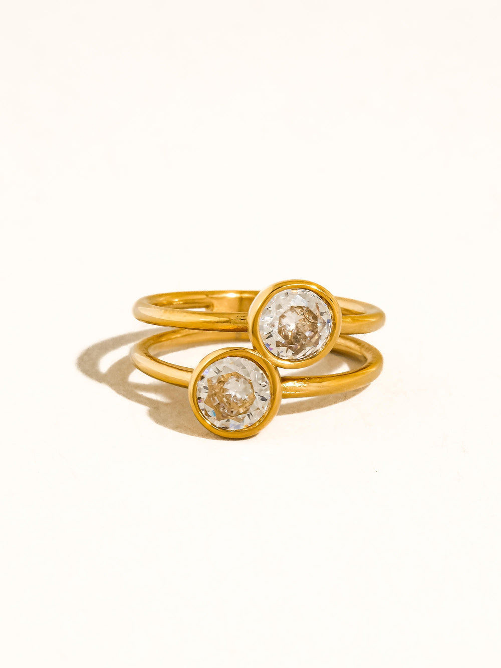 The Double CZ Bezel Stacked Ring in 18K Gold - Product Flat Lay on Cream Background Showing Front View of Double Band with Two Round CZ Bezel Stones Side by Side