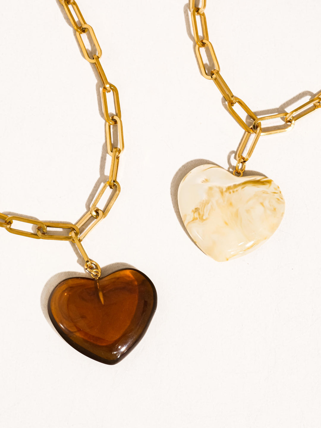 The Resin Heart Paperclip Chain Necklace in 18K Gold - Product Shot on Cream Background Showing Both Colorways Side by Side — Amber Tortoise Heart (Left) & Cream Marble Heart (Right) on Chunky Gold Paperclip Chain