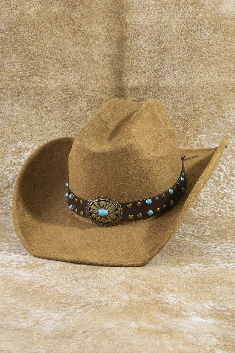 The Turquoise Concho Studded Cowboy Hat in Tan - Three-Quarter View on Cowhide Surface Showing Warm Tan Suede Felt Body, Dark Leather Studded Hatband with Scattered Turquoise Stones & Central Bronze Floral Concho