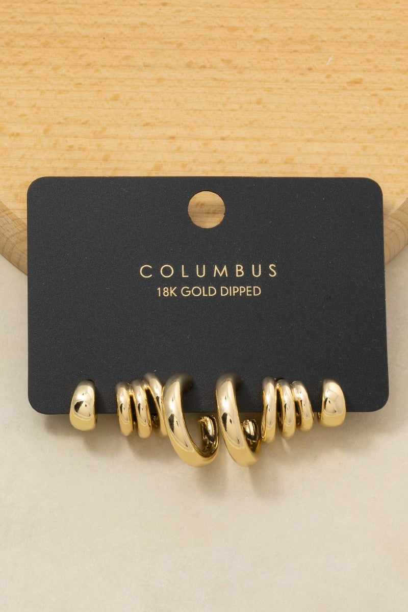 The Columbus Triple Coil Hoop Earrings in 18K Gold Dipped - Product Shot on Black Columbus Card Against Wood Background Showing Full 4-Pair Hoop Set Including Triple Coil Style