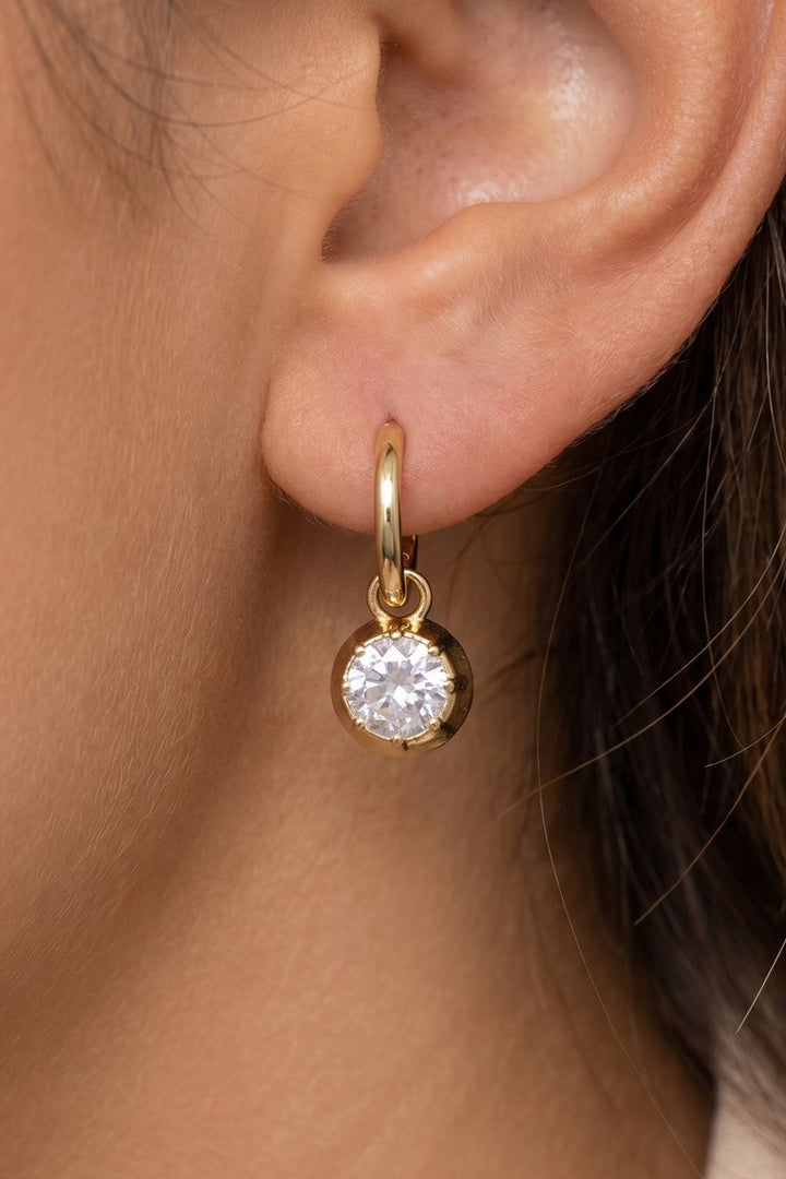 The Columbus CZ Bezel Charm Huggie Earrings in Gold Dipped - On-Model Close-Up Showing Single Earring Worn on Ear with Gold Click-Top Huggie Hoop & Round CZ Bezel Charm Swinging Below