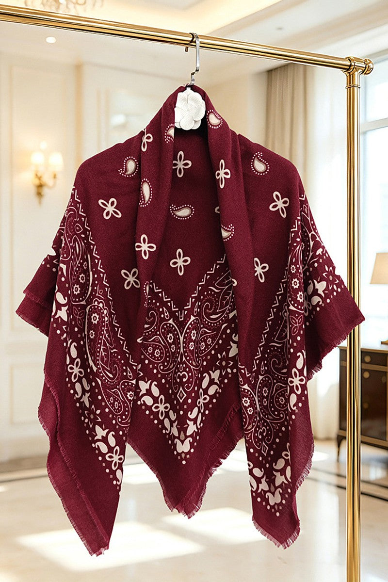 A burgundy bandana-style shawl with white paisley and floral prints, hanging on a gold clothing rack in a bright, elegant room.