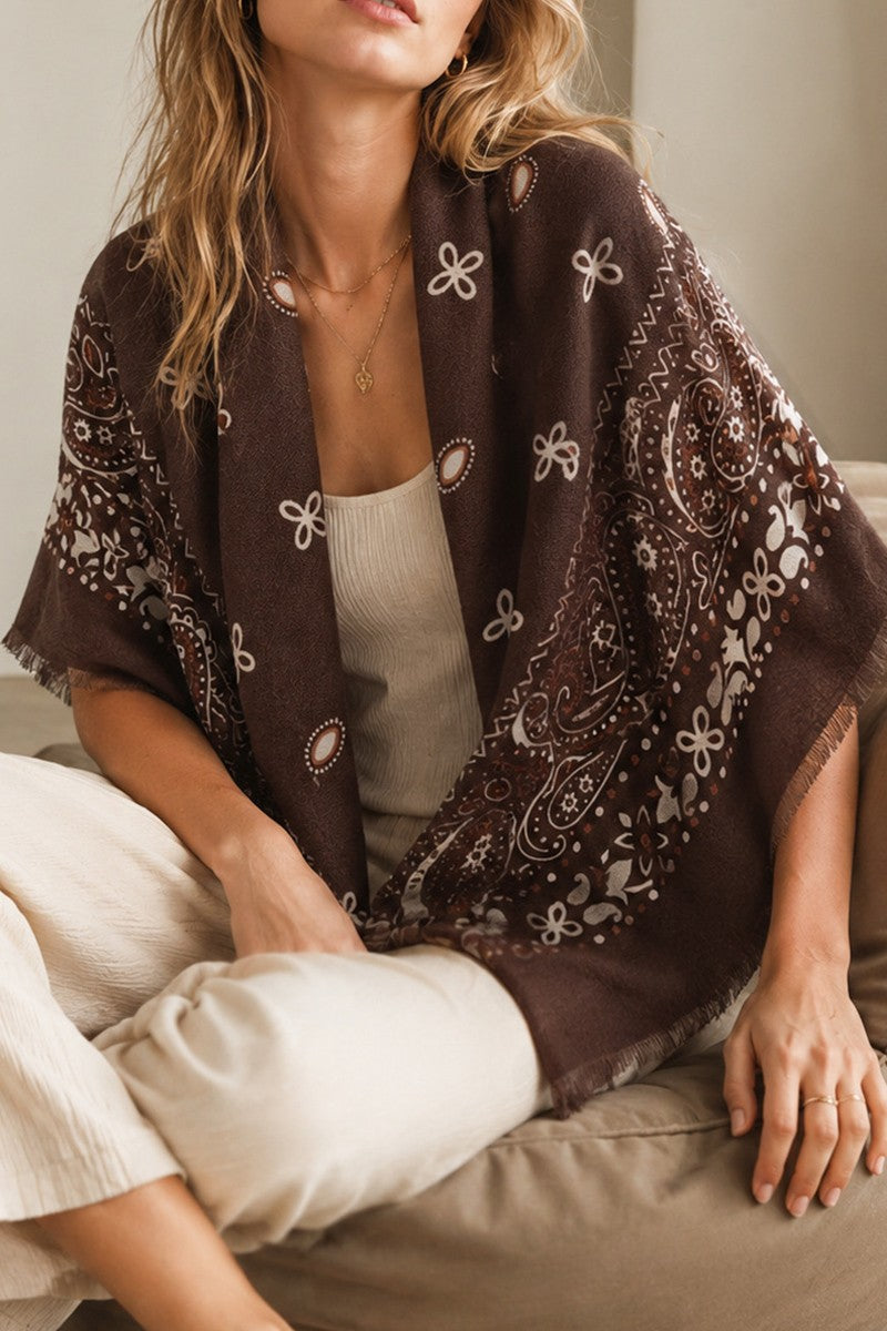Brown scarf shawl with ivory paisley and floral print and fringed edges, draped over a cream tank and neutral trousers