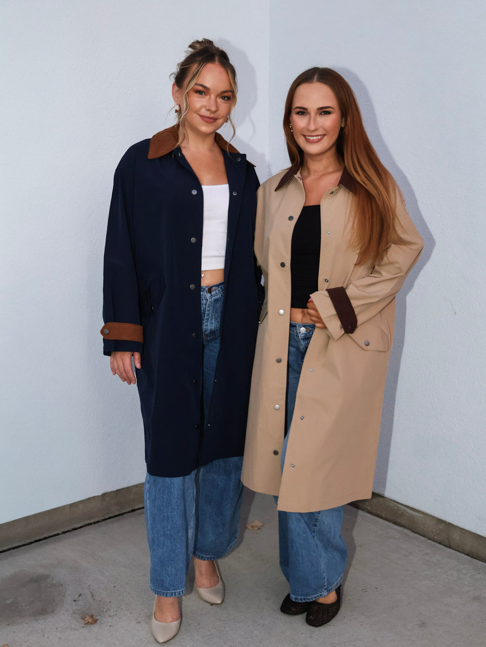 Two women standing side by side wearing long coats against a plain background