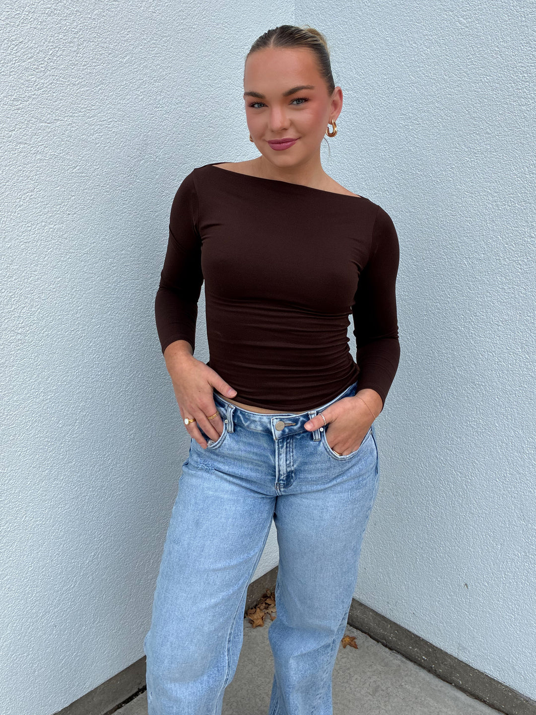 Person wearing a brown long-sleeve top and light blue jeans against a light blue wall.
