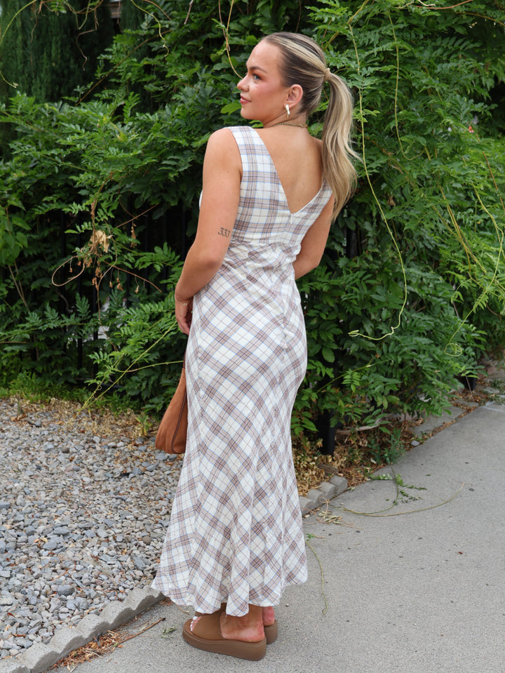 Woman wearing a plaid dress standing outdoors with greenery in the background