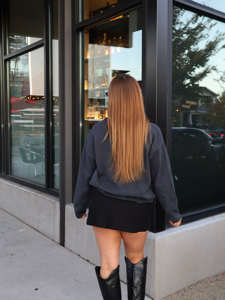 Person wearing a dark jacket and black skirt standing in front of a glass door.
